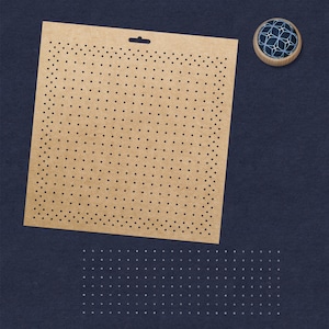 May include: A tan perforated craft sheet with a hanging hole, and a wooden-rimmed button with a blue geometric design. The sheet is covered in evenly spaced black dots. The background is a dark blue.