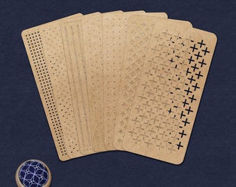 May include: A set of six rectangular tan craft templates featuring various laser-cut patterns including dots, lines, and plus signs, arranged in a fan shape, accompanied by a small round wooden pincushion with a blue and white geometric fabric top.
