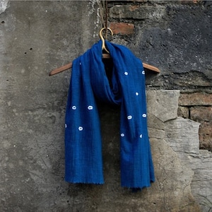 Peut inclure: Une écharpe bleue à pois blancs accrochée à un cintre en bois sur un mur gris texturé.
