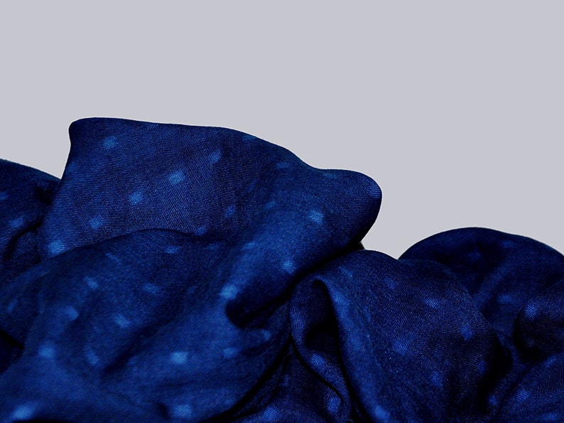 May include: A blue fabric with a white polka dot pattern. The fabric is folded and draped, creating a soft and textured look.
