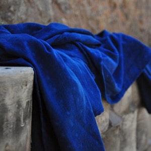 May include: A deep blue fabric draped over a stone wall. The fabric is folded and bunched up, creating a textured look.