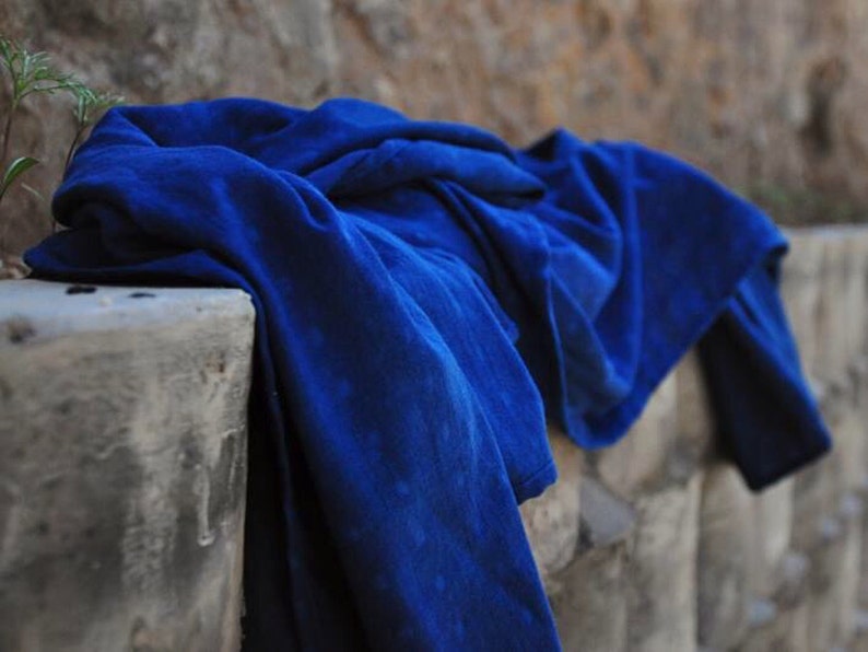 May include: A deep blue fabric draped over a stone wall. The fabric is folded and bunched up, creating a textured look.
