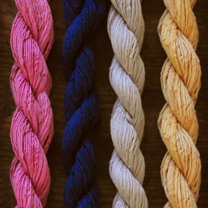 May include: Close-up of seven strands of yarn in different colors: yellow, pink, dark blue, gray, light yellow, and gray. The yarn is twisted and arranged vertically.