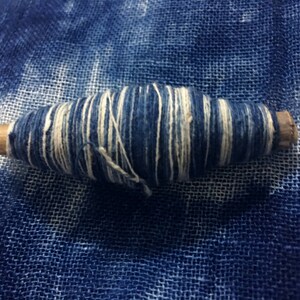 May include: A spool of blue and white thread wrapped around a wooden dowel. The thread is wound tightly and has a striped pattern.