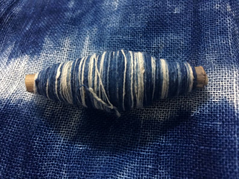 May include: A spool of blue and white thread wrapped around a wooden dowel. The thread is wound tightly and has a striped pattern.