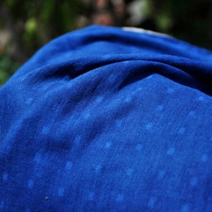 May include: A close-up of a blue fabric with a white speckled pattern. The fabric is soft and textured, with a slightly wrinkled appearance.