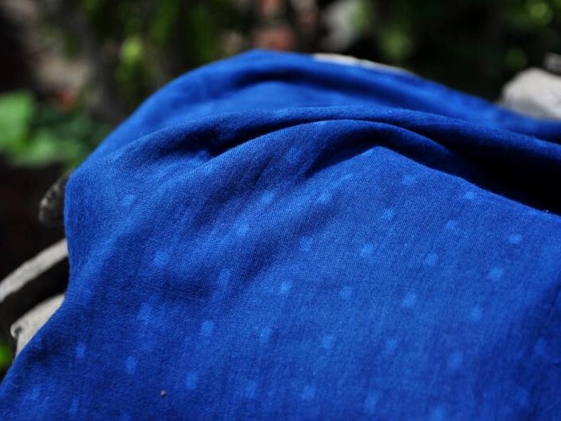 May include: A close-up of a blue fabric with a white speckled pattern. The fabric is soft and textured, with a slightly wrinkled appearance.