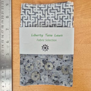May include: A sample of Liberty Tana Lawn fabric with a geometric pattern on one side and a floral pattern on the other. The fabric is labelled "Liberty Tana Lawn Fabric Selection".