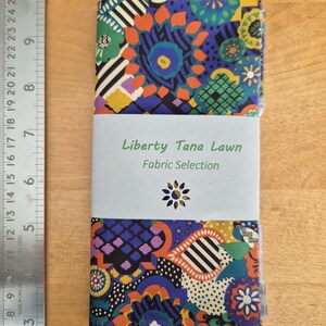 May include: A stack of Liberty Tana Lawn fabric samples with a vibrant floral design in blue, orange, green, and purple. The fabric is wrapped with a light blue band that reads "Liberty Tana Lawn Fabric Selection".