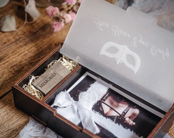 May include: A wooden box with a black finish and a clear lid. The box contains a wooden USB drive with the word "Memories" engraved on it, a white ribbon, and a photograph. The lid has the text "Your Story Told Our Way" written on it.