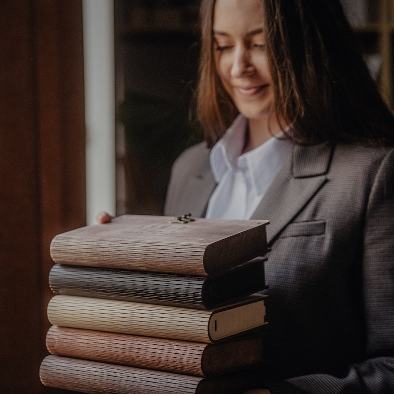 May include: A stack of six brown, black, and beige journals with a wooden cover. The journals are bound with a metal clasp and have a textured surface.