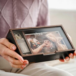 Hands holding closed black wooden photo box with clear engraved acrylic lid, personalized keepsake gift.