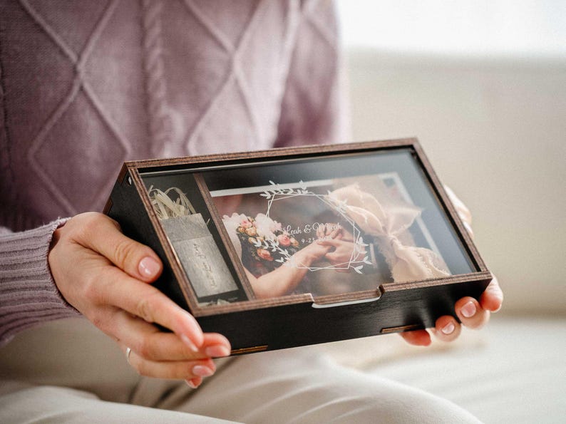 Hands holding closed black wooden photo box with clear engraved acrylic lid, personalized keepsake gift.