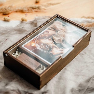 Closed walnut wooden photo box with clear engraved acrylic lid on fabric background, gift-ready keepsake for 4x6 photos.
