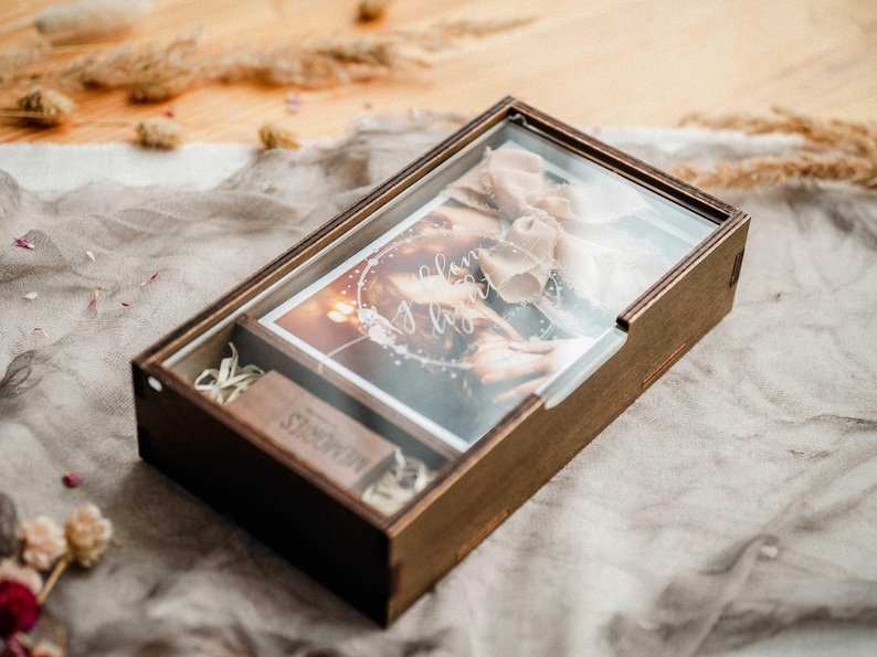Closed walnut wooden photo box with clear engraved acrylic lid on fabric background, gift-ready keepsake for 4x6 photos.