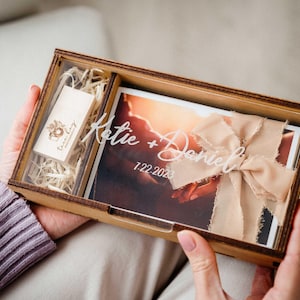 Hands holding open photo box showing engraved lid, 4x6 print storage and USB slot for photographer delivery.