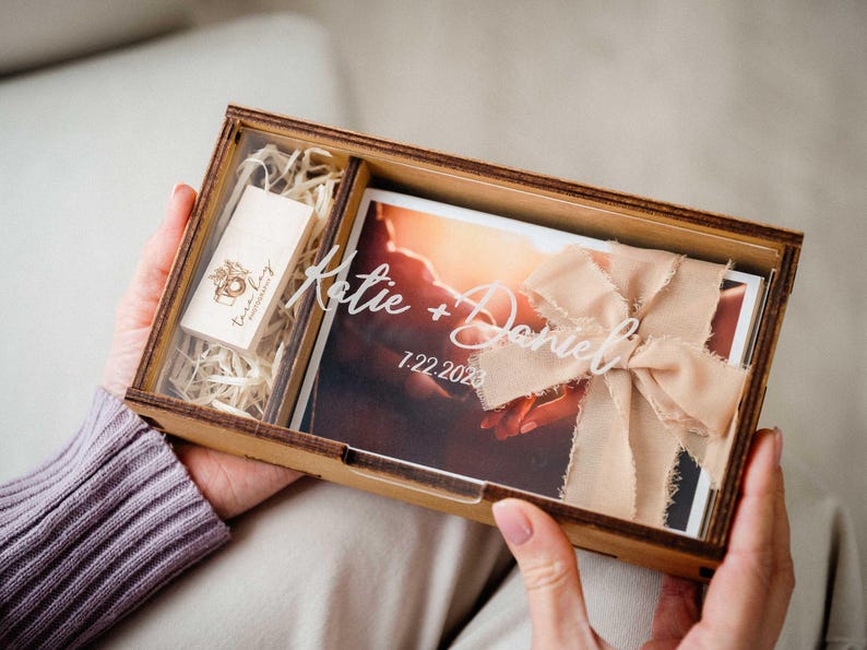 Hands holding open photo box showing engraved lid, 4x6 print storage and USB slot for photographer delivery.