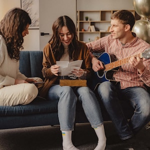 Family opening a personalized wooden photo box together on a couch, looking at printed photos.