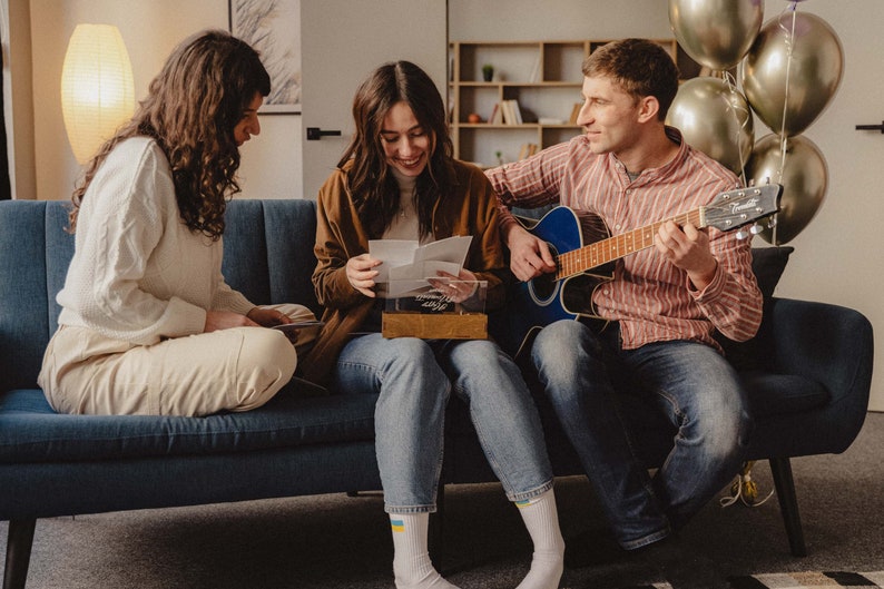 Family opening a personalized wooden photo box together on a couch, looking at printed photos.