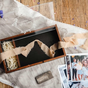 Top view of open photo box with 4x6 prints, ribbon and wood shavings in a styled flat lay scene.