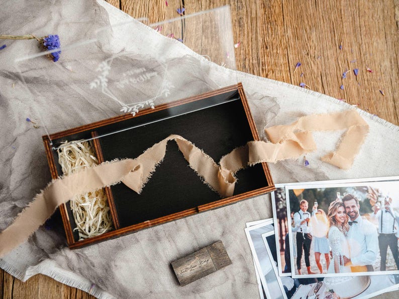 Top view of open photo box with 4x6 prints, ribbon and wood shavings in a styled flat lay scene.