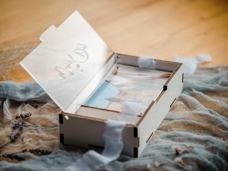 White wooden photo box open with clear engraved acrylic lid and 4x6 prints, ribbon styling.
