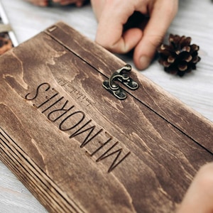 May include: A dark brown wooden box with a latch and the word "MEMORIES" engraved on the front. The box is made of layered wood and has a rustic look.