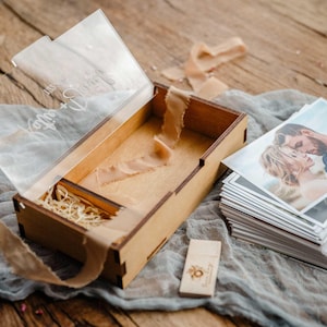 Open photo box with USB compartment beside a stack of 4x6 prints and wooden USB stick on table.