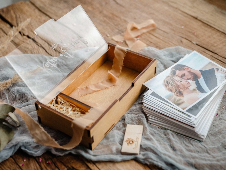 Open photo box with USB compartment beside a stack of 4x6 prints and wooden USB stick on table.