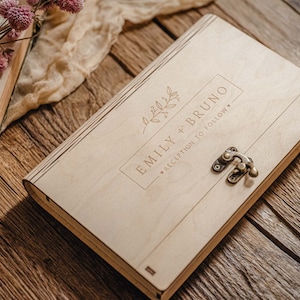 May include: A wooden box with a latch closure. The box is engraved with the text "Emily + Bruno" and "Reception to follow".