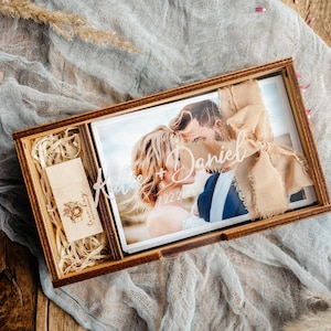 Top-down walnut photo box with engraved acrylic lid, 4x6 photos and USB compartment on linen fabric.
