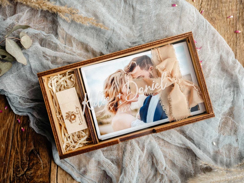 Top-down walnut photo box with engraved acrylic lid, 4x6 photos and USB compartment on linen fabric.