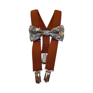May include: Rust-colored suspenders with silver-tone clips and a floral patterned bow tie. The bow tie features a blue background with small white and yellow flowers. The suspenders are made of a sturdy, elastic material.