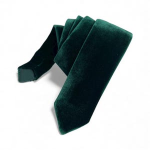 May include: A deep emerald green velvet tie, folded and displayed against a white background. The tie has a soft, plush texture and a classic pointed end. The fabric appears to be high-quality, suitable for formal wear or special occasions.