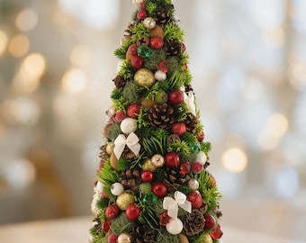 May include: A conical tabletop Christmas tree decoration featuring a woven star topper, green foliage, brown pinecones, red berries, and small gold, red, and white ornaments. The tree is accented with tiny white bows and textured moss elements.