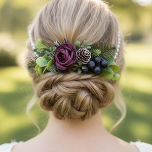 May include: A hair accessory featuring a deep burgundy fabric rose, a small pinecone, dark blue berries, and green foliage. The piece is attached to a white pearl headband and is positioned above a braided bun hairstyle with loose strands.