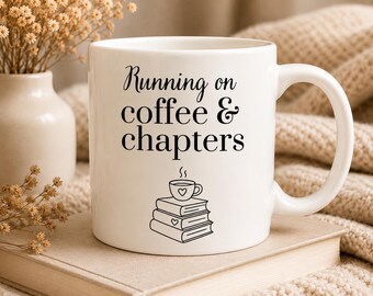 Pode incluir: Caneca de cerâmica branca com o texto "Running on coffee & chapters" em escrita preta. A caneca apresenta uma pilha de livros com uma chávena de café em cima. A caneca está em cima de um livro.