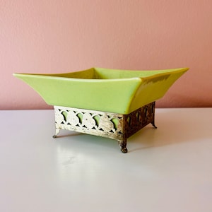 May include: A square, lime green ceramic bowl with a silver metal stand. The stand has a decorative, openwork design.