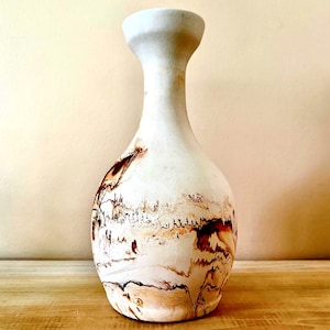 May include: A white ceramic vase with brown and orange marbling. The vase has a round body and a narrow neck.