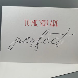 May include: White card with red text that says "To me, you are" and black cursive text that says "perfect".