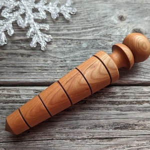 May include: A handcrafted wooden bottle stopper with a light brown finish. The stopper features a rounded top, a cylindrical body with four grooved rings, and a tapered end. The design is simple and elegant, suitable for wine bottles.