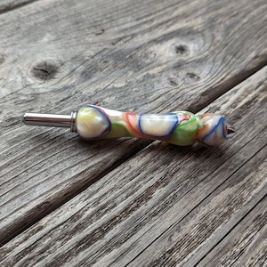 May include: A colorful crochet hook with a silver metal tip and a white, green, blue, orange, and red swirl pattern.
