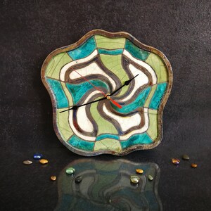 May include: A ceramic clock with an abstract design in green, blue and white. The clock has a black hour hand and a red minute hand.
