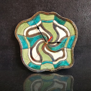 May include: A ceramic clock with a green, blue and white abstract design. The clock has a wavy, irregular shape and black hands.