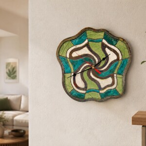 Pu&ograve; includere: Un orologio da parete dalla forma irregolare e organica con un motivo segmentato di sezioni verdi, verde acqua e bianco sporco con contorni scuri. L'orologio presenta due lancette nere e una lancetta dei secondi rossa sul quadrante.