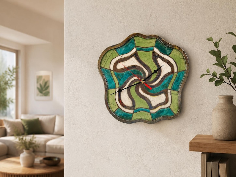 Pu&ograve; includere: Un orologio da parete dalla forma irregolare e organica con un motivo segmentato di sezioni verdi, verde acqua e bianco sporco con contorni scuri. L'orologio presenta due lancette nere e una lancetta dei secondi rossa sul quadrante.