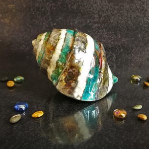 Puede incluir: Concha decorativa de cer&aacute;mica con acabado brillante. La concha presenta un patr&oacute;n a rayas en blanco, turquesa, marr&oacute;n y dorado. Peque&ntilde;as cuentas de vidrio de colores rodean la concha. Un art&iacute;culo de decoraci&oacute;n del hogar &uacute;nico.