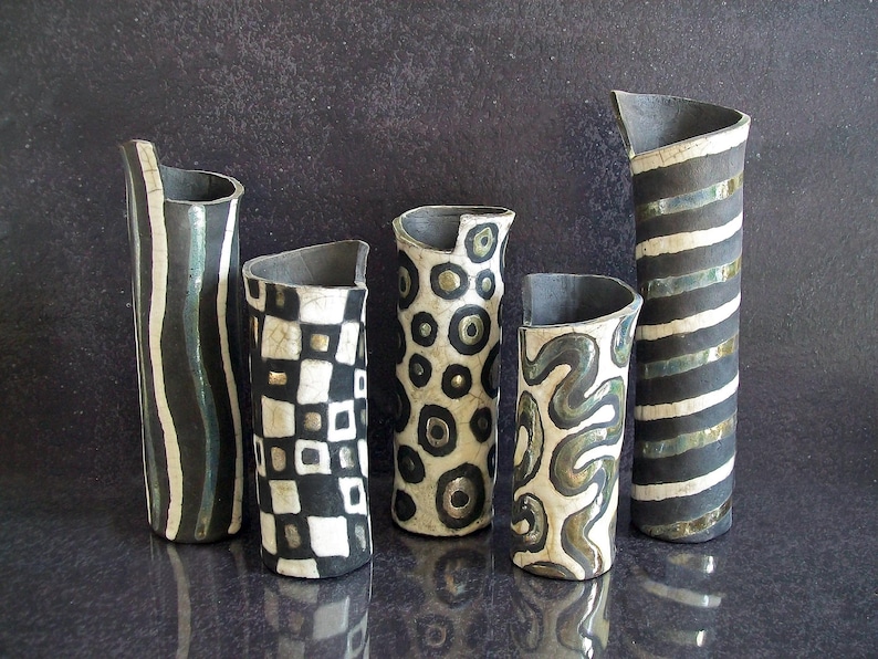 May include: Five ceramic vases with unique designs. The vases are cylindrical with asymmetrical tops. Patterns include vertical stripes, wavy lines, checkerboard, and circles. The color palette is primarily black, white, and gray.