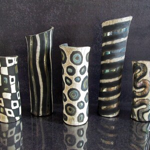 May include: Five handcrafted ceramic vases with unique designs. The vases feature black and white patterns, including stripes, circles, and geometric shapes. Each vase has a different shape and size, adding to their artistic appeal.