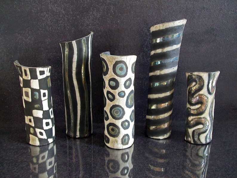 May include: Five handcrafted ceramic vases with unique designs. The vases feature black and white patterns, including stripes, circles, and geometric shapes. Each vase has a different shape and size, adding to their artistic appeal.